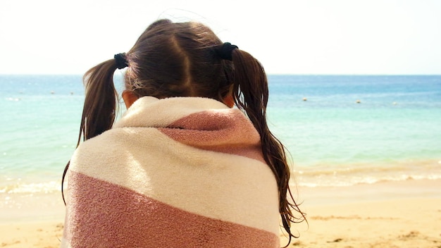 Kleines Mädchen mit zwei Pferdeschwänzen in ein Handtuch gewickelt am Strand