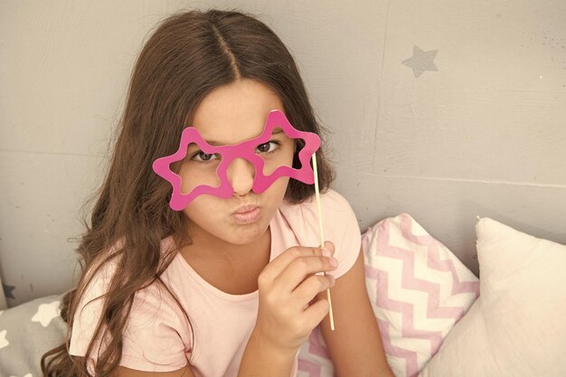 Kleines Mädchen Party Brille Pyjama Party bereit für Spaß lustiger Look von kleinen Kindern Kindheitsmomente internationaler Kindertag ernstes Kind in Sternbrille guten Morgen will nicht schlafen