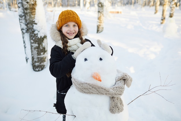 Kleines Mädchen posiert mit Schneemann