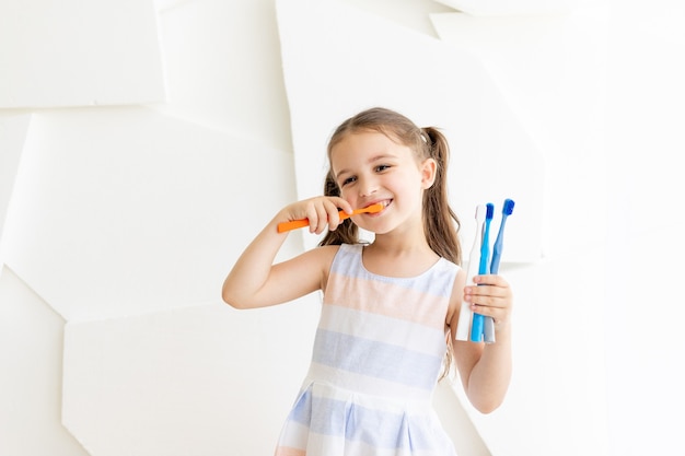 kleines Mädchen putzt sich die Zähne und hält Zahnbürsten