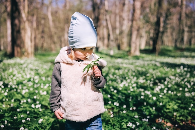 Kleines Mädchen riecht weiße Anemonenblüten im Wald