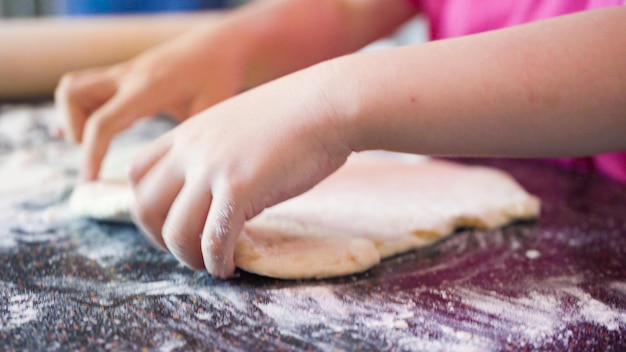 Kleines Mädchen rollt Pizzateig für einzelne kleine Pizzen aus.