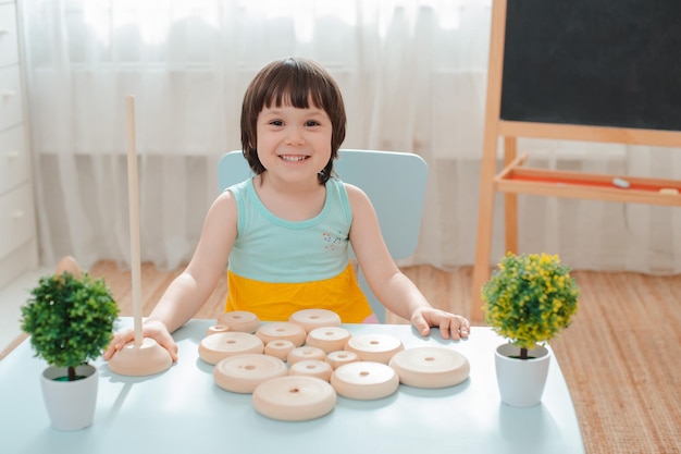 Kleines Mädchen sammelt eine unbemalte Holzpyramide. Sicheres Kinderspielzeug aus Naturholz