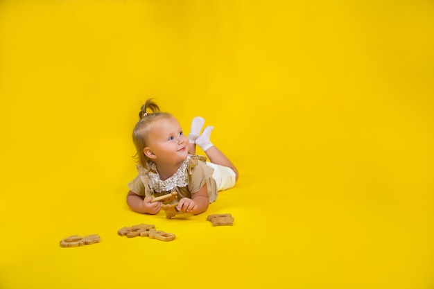 kleines Mädchen schaut in die Ferne liegt auf gelbem Hintergrund mit Holzspielzeug