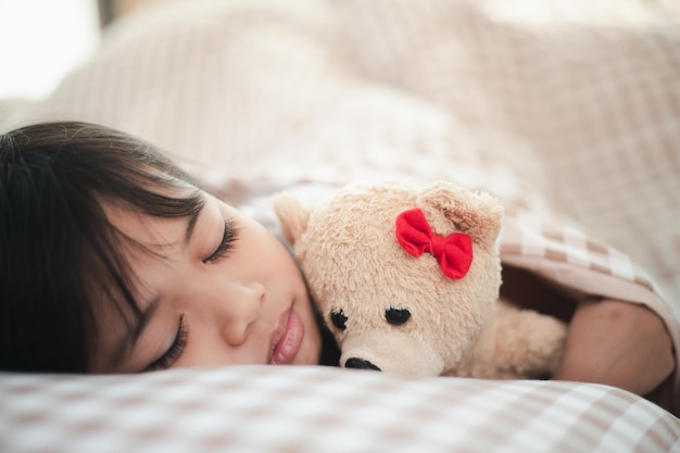 Kleines Mädchen schläft im Bett mit einem Spielzeug-Teddybär