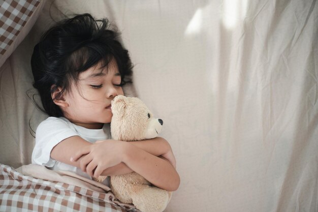 Kleines Mädchen schläft im Bett mit einem Spielzeug-Teddybär