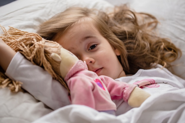 kleines Mädchen schläft im Bett mit weicher Puppe weiß ein