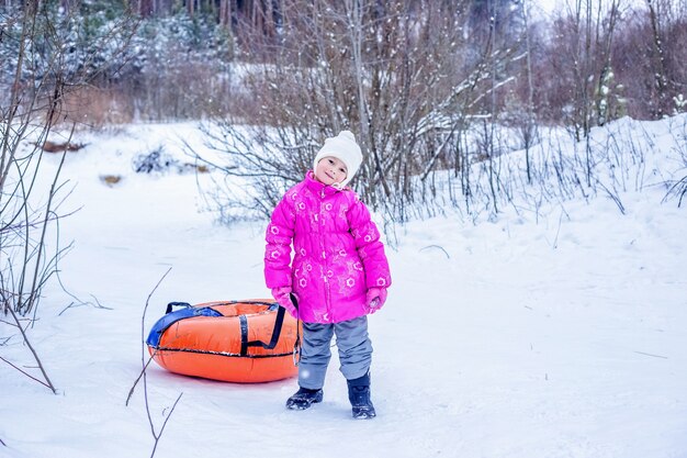 Kleines Mädchen schleppt Slide-Slide-Käsekuchen den schneebedeckten Hügel hinauf. Konzept der Winteraktivitäten im Freien für Kinder.