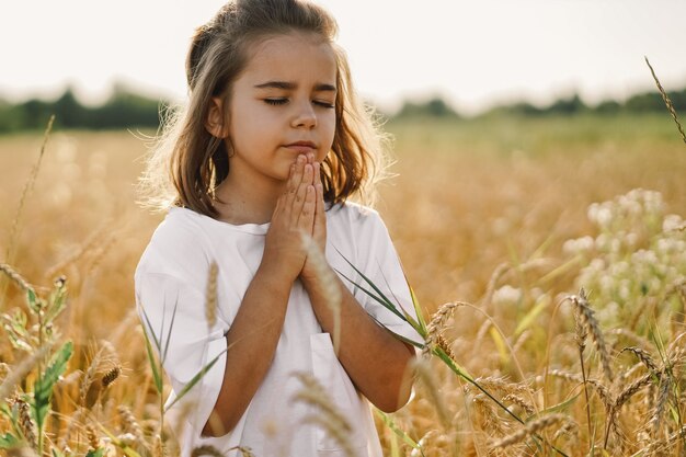 Kleines mädchen schloss die augen und betete in einem feldweizen. hände im gebet gefaltet. religionskonzept