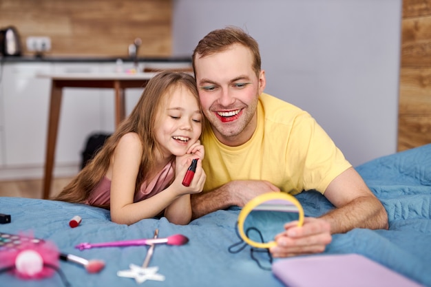 kleines Mädchen schminken ihren jungen Vater. Papa verbringt ihre Freizeit mit ihrer Tochter zu Hause.