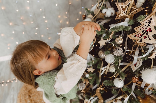 Kleines Mädchen schmückt den Weihnachtsbaum mit Spielzeug. Ein süßes Baby bereitet sich zu Hause auf die Weihnachtsfeier vor.