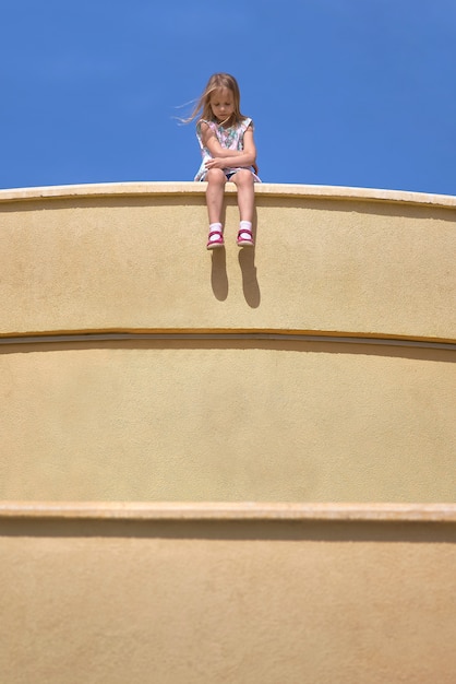 Foto kleines mädchen sitzt am rand der wand baumelnden beinen, steinmauer baumelt ihre beine in der luft