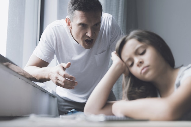 Kleines Mädchen sitzt am Tisch, während Vater schreit