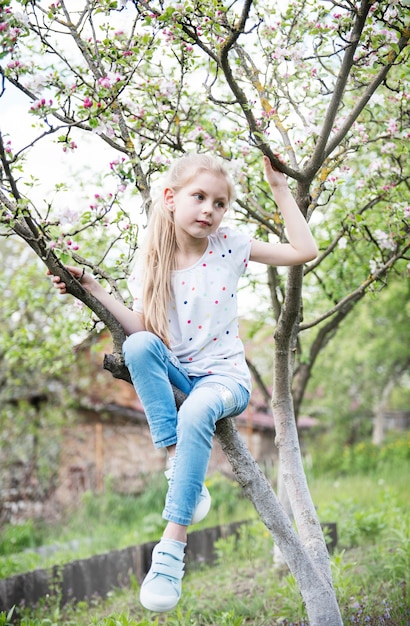 Kleines Mädchen sitzt auf blühendem Baum im Apfelgarten