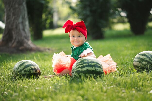 Kleines Mädchen sitzt auf dem grünen Gras in einem roten Tüllrock mit Wassermelonen