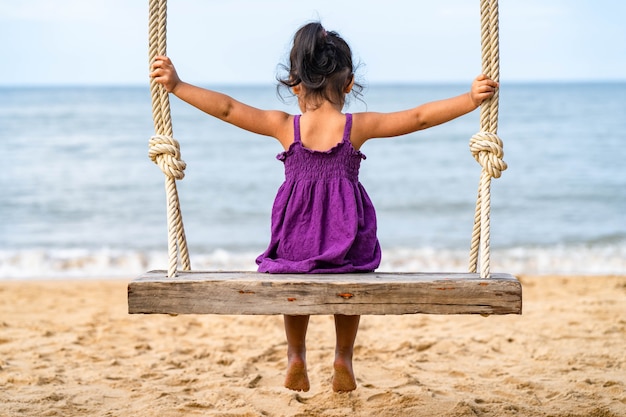 kleines Mädchen sitzt auf der Holzschaukel am Strand.