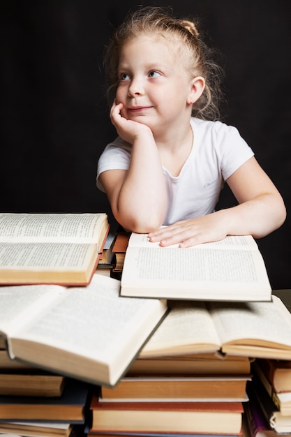 kleines Mädchen sitzt auf einem Stapel Bücher und Träume. Schul-und Berufsbildung.