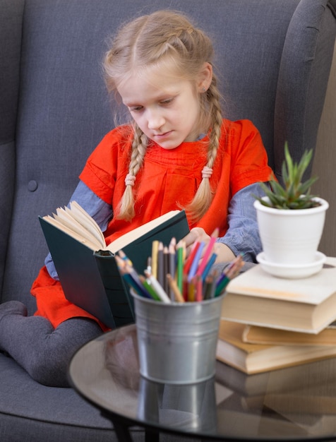 Kleines Mädchen sitzt auf einem Stuhl und liest ein Buch