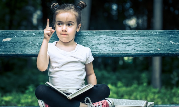 kleines Mädchen sitzt auf einer Bank und liest ein Buch