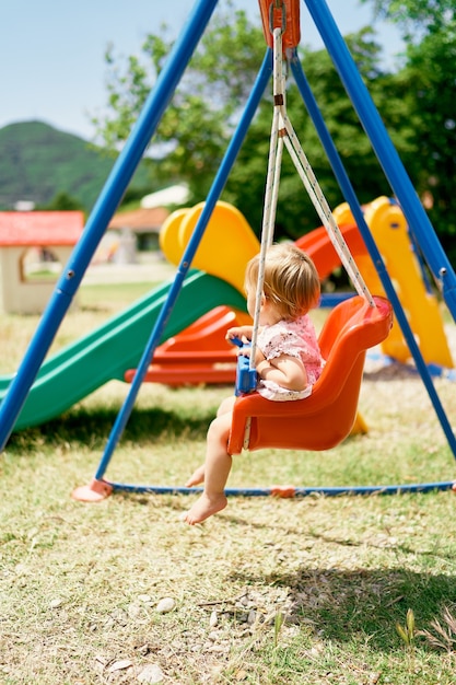 Kleines Mädchen sitzt auf einer Schaukel in der Seitenansicht des Parks