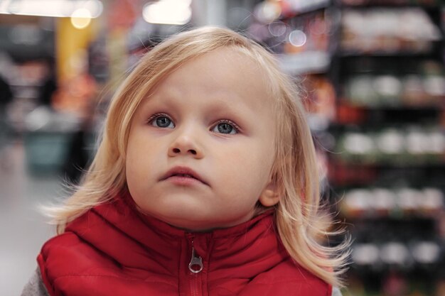 Kleines Mädchen sitzt im Einkaufswagen im Laden oder Supermarkt und kauft