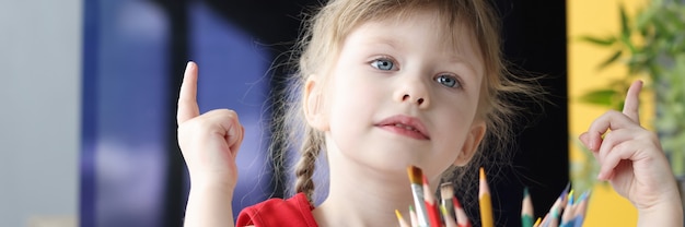 Kleines Mädchen sitzt mit Bleistiften am Tisch und zählt Zahlen an ihren Fingern. Bildungskonzept für Vorschulkinder