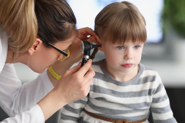 Kleines Mädchen sitzt ruhig, während der Hausarzt die Ohren mit spezieller Ausrüstung untersucht