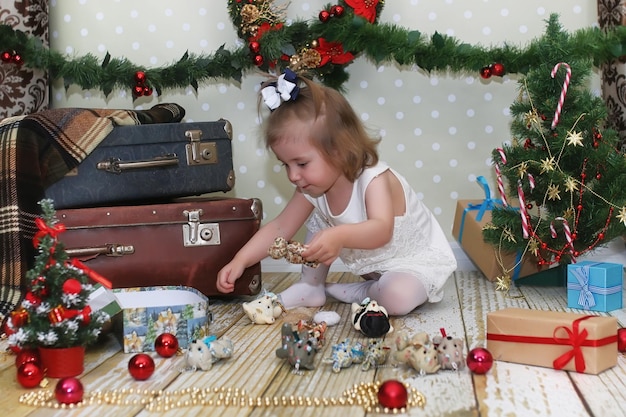 Kleines Mädchen sitzt vor einem Weihnachtsbaum und spielt mit Spielzeug