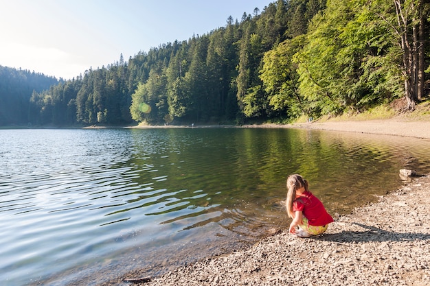 kleines Mädchen spielt am Ufer eines Bergsees