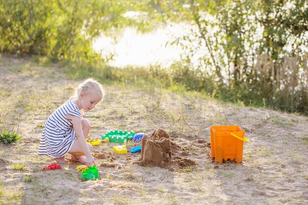 Kleines Mädchen spielt auf Sand mit Spielzeugen am Fluss