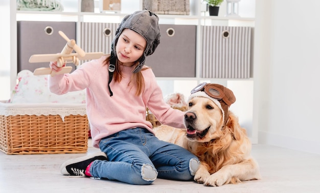 Kleines Mädchen spielt im Flugzeugpiloten mit Golden Retriever Hund