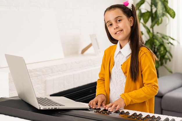 kleines mädchen spielt klavier in der klassenbildung mit laptop beim online-lernen zu hause in der covid-19-krisenquarantäne.