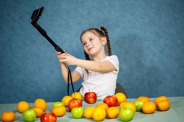 Kleines Mädchen spielt mit Früchten und macht ein Selfie am Telefon. Vitamine und gesunde Ernährung für Kinder.