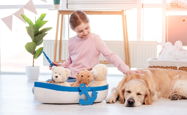 Kleines Mädchen spielt mit Seeschiff und streichelt Golden Retriever Hund, der in ihrer Nähe schläft