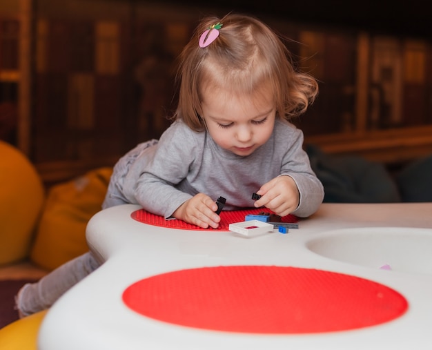 Kleines Mädchen spielt Spielzeugsteine am Tisch im Kinderunterhaltungszentrum