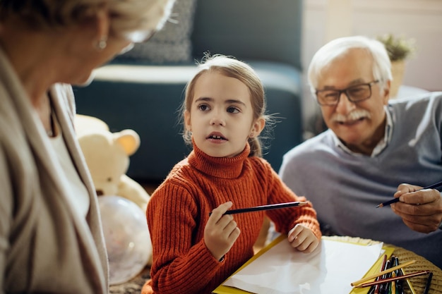 Kleines Mädchen spricht mit Großeltern, während es zu Hause auf dem Papier zeichnet