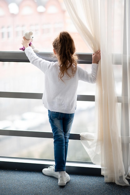 Foto kleines mädchen steht in der nähe eines fensters mit teddybär in ihren händen lifestile der kindheit