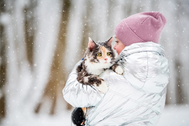 Kleines Mädchen trägt eine Katze in ihren Armen in einem schneereichen Winter