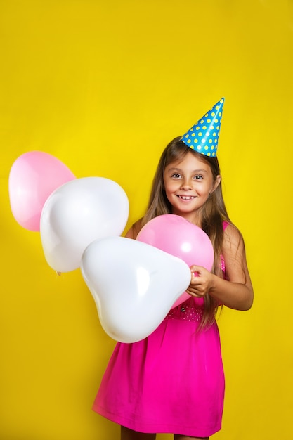 kleines Mädchen trägt einen Partyhut an ihrem Geburtstag. Glückliches Mädchen mit bunten Ballonen