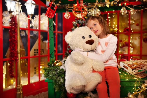 Kleines Mädchen träumt von Wundern zu Weihnachten Schönes Kind umarmt Spielzeug Teddybär Weihnachtsdekoration