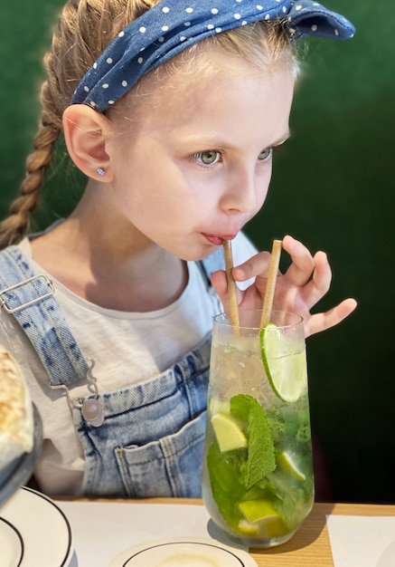 Kleines Mädchen trinkt alkoholfreien Mojito in einem Café