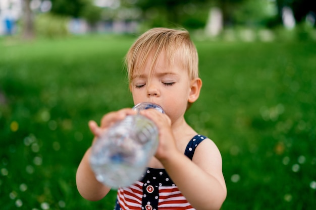 Kleines Mädchen trinkt Wasser aus einer Flasche, die ihre Augen schließt