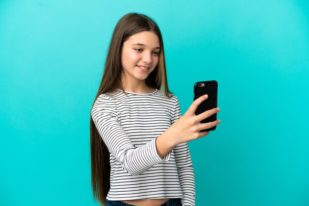 Kleines Mädchen über isoliertem blauem Hintergrund macht ein Selfie