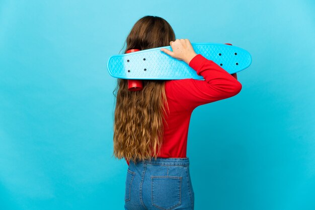 Kleines Mädchen über isoliertem blauem Hintergrund mit einem Schlittschuh in der hinteren Position