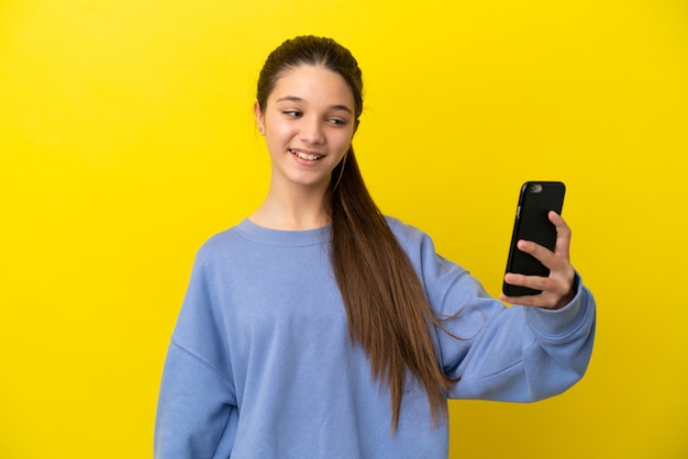 Kleines Mädchen über isoliertem gelbem Hintergrund macht ein Selfie mit dem Handy