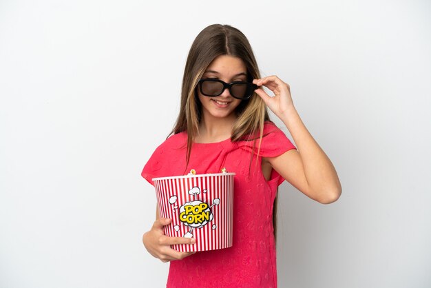 Kleines Mädchen über isolierter weißer Wand mit 3D-Brille und hält einen großen Eimer Popcorn