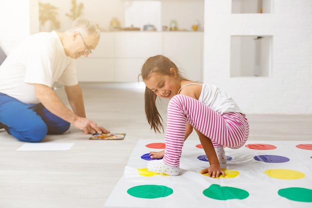 kleines Mädchen und Großvater spielen Twister zu Hause