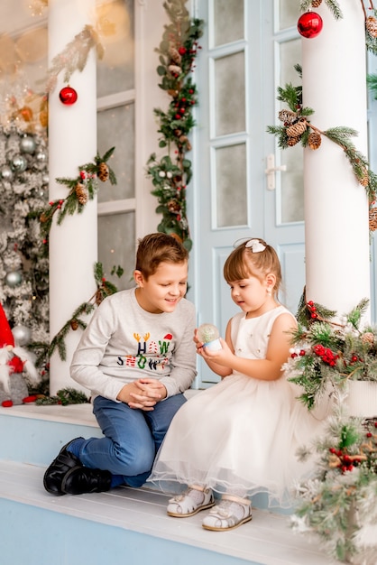 Kleines Mädchen und ihr Bruder öffnen Weihnachtsgeschenke. Kinder sehen eine Überraschungsschneekugel