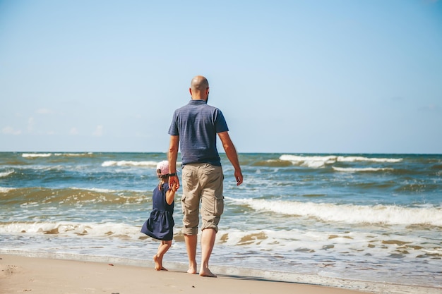 Kleines Mädchen und ihr Vater halten sich an den Händen, während sie die Wellen am Strand einer Ostsee beobachten