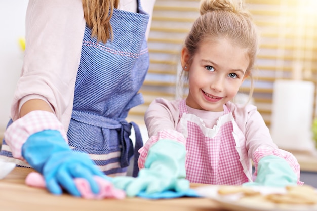 kleines Mädchen und ihre Mutter in Schürzen haben Spaß beim Putzen der Küche